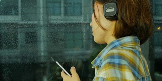 女士用手机听音乐。外面在下雨，侧视图。从右到左。