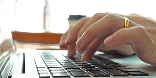 在家工作，用笔记本电脑写博客。咖啡店里男性的手在敲击键盘。