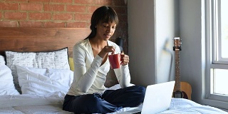 年轻的非洲裔美国女性在床上喝着咖啡和笔记本电脑