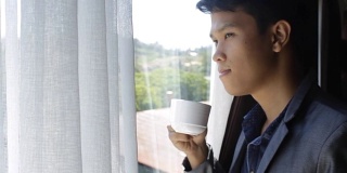 一个亚洲人看着窗外，喝着茶