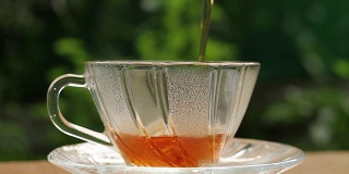 在泰国清晨的阳光下，将热茶倒入绿色的玻璃茶杯中