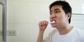 一名亚洲男子早上在浴室对着镜子刷牙