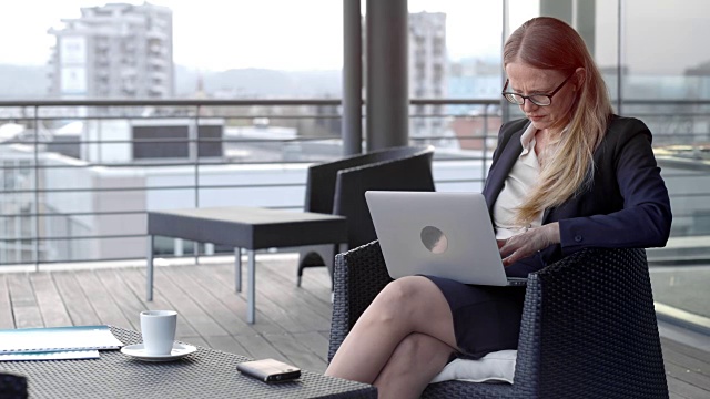白种女商人戴着眼镜在城市的屋顶休息室里用笔记本电脑工作