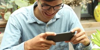 年轻的亚洲快乐男子坐在公园里用智能手机