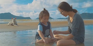 亚洲年轻的母亲和她的女儿和一只狗在海滩上玩耍