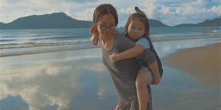 亚洲年轻母亲和小女儿在海滩上玩耍