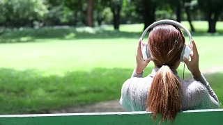 亚洲女人在公园里听音乐放松视频素材模板下载