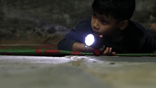 一个小男孩拿着电筒在黑暗中寻找。