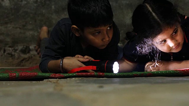 一个小男孩和一个小女孩拿着手电筒在黑暗中寻找。