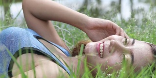 年轻美丽的女人微笑着躺在夏天的草地上
