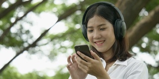 亚洲年轻女性听音乐与无线耳机在秋季公园-播客