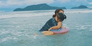 亚洲年轻的母亲和她的女儿拥抱和玩在海滩上的海浪