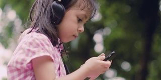 一个小女孩坐在泰国的公园里，戴着耳机听播客