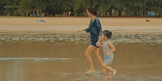 亚洲年轻母亲和她的小女儿在海滩上跑步