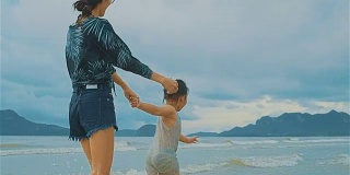 亚洲年轻母亲和她的小女儿在海边跑步