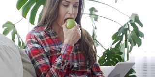 侧面的漂亮女性一边吃苹果一边用平板电脑