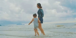 亚洲年轻母亲和她的小女儿在海边跑步