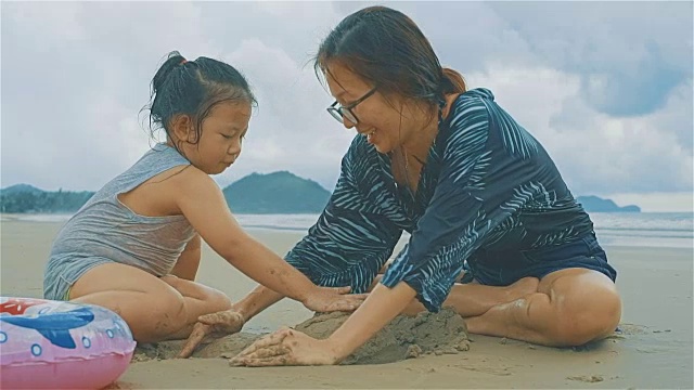 亚洲年轻的母亲和她的女儿在沙滩上玩沙子