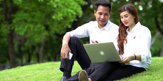 4K视频亚洲商人和女商人与休闲西装在户外公园与科技笔记本电脑工作