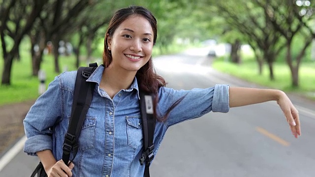 亚洲女性与明亮的背包和自由旅行者女人站着举起手臂，享受美丽的自然