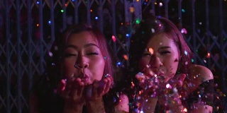 慢镜头里，两个女孩在派对上用手吹五彩纸屑