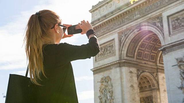 年轻的女游客走在巴黎的街道上，拍下凯旋门的照片