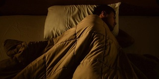 一名沮丧的男子因失眠躺在床上的画面