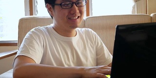 快乐的亚洲人在休闲衣服使用笔记本电脑和喝咖啡在客厅-室内场景