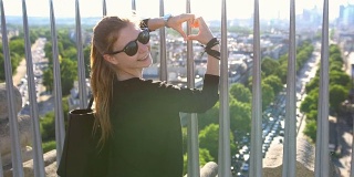 一名女子站在巴黎凯旋门上，双手搭成心形，俯视着整个城市