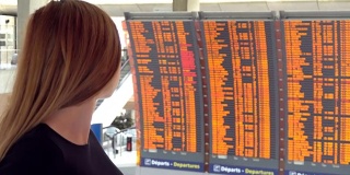 一个女人在机场看飞机航班信息板