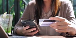 近距离观察年轻的亚洲女性用信用卡在手机上购物