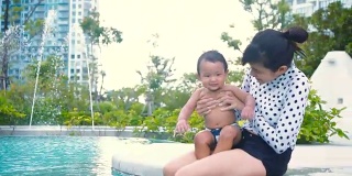 年轻的母亲和儿子坐在游泳池里