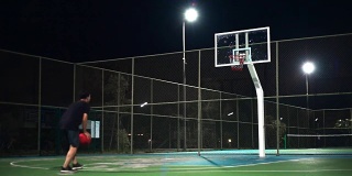 运动概念:一个人晚上独自在室外打篮球。
