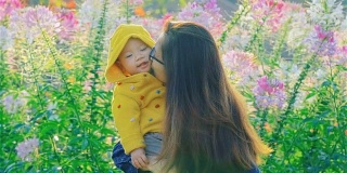 在公园里，母亲把婴儿举到空中，亲吻女孩的脸颊