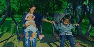 年轻的母亲和两个女儿在公园的摇椅上享受大自然