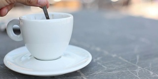 在室外的大理石咖啡桌上搅拌一杯新鲜的咖啡