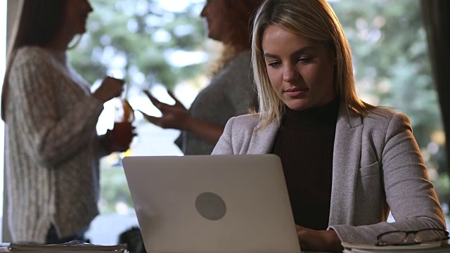 一位年轻的女商人在和朋友们聊天后在电脑上输入电子邮件。