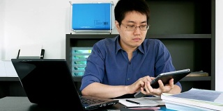 戴眼镜的亚洲商人在家庭办公室使用笔记本电脑和平板电脑