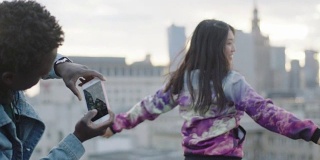 快乐的年轻亚洲女人在屋顶上摆姿势与摄影师与智能手机