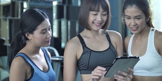年轻的亚洲人在健身房看平板电脑与健身教练，慢动作