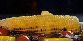 玉米和融化的黄油放在燃烧的烤架上