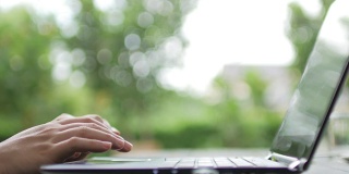 女人用绿色散焦背景的笔记本电脑键盘打字，在家工作