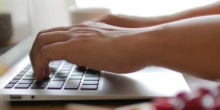 人类的双手在笔记本电脑键盘上打字，木桌上有在家工作的元素，多莉从右向左射击
