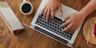 人类的双手在笔记本电脑键盘上打字，木桌上有在家工作的元素，多莉从右向左射击
