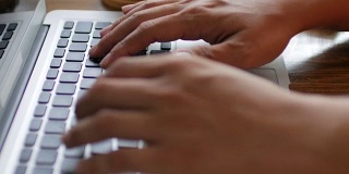 人类的双手在笔记本电脑键盘上打字，木制的桌子上有在家工作的元素，多莉拍摄倾斜