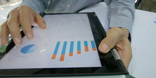 商人检查和分析数字平板电脑上的图表，摄影车从右向左拍摄