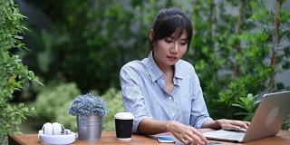 亚洲年轻女子坐在工作场所，在花园里使用笔记本电脑