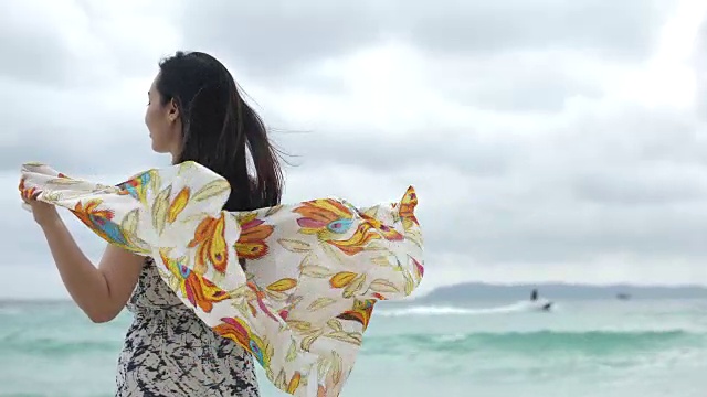年轻快乐的女人戴着围巾在海滩上，慢镜头