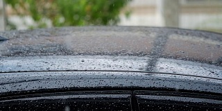 下雨的一天。雨水落在停在路上的黑色汽车的车顶上。