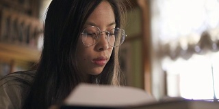 年轻的亚洲妇女坐在图书馆的桌子旁看书的肖像